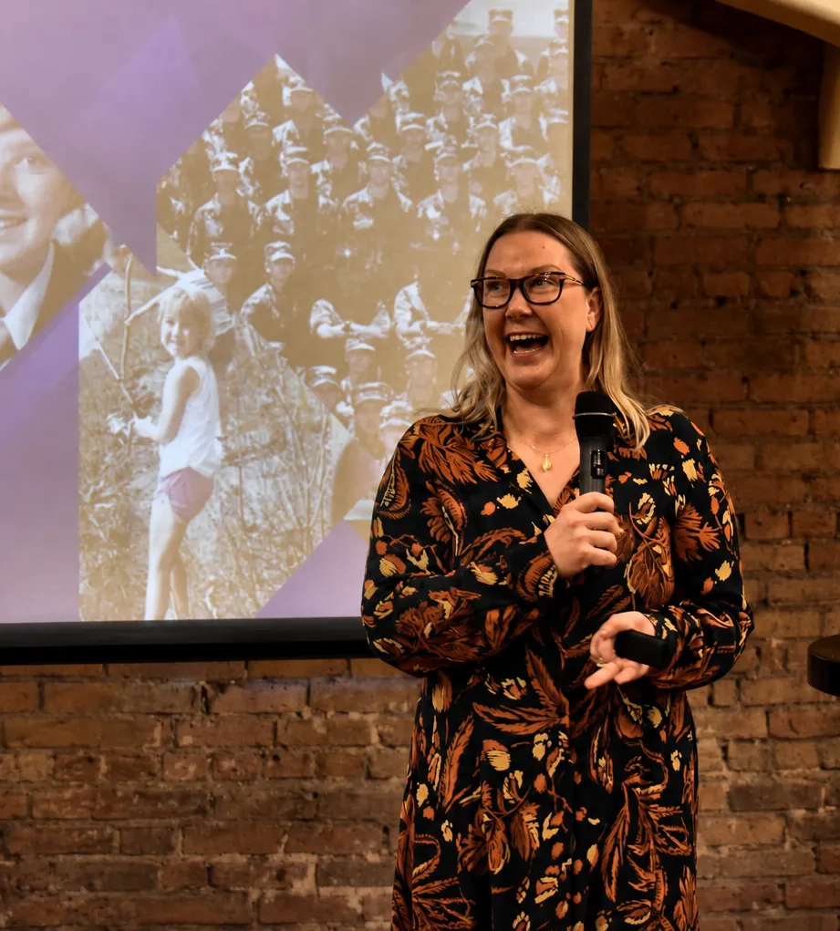 Lea Greene laughing while speaking on stage, holding a microphone